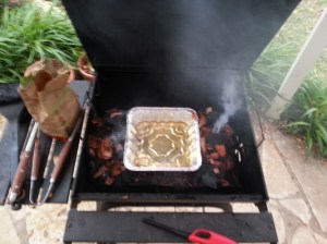 Prepping the grill. A drip pan full of Lone Star surrounded by two piles of a hardwood charcoal/mesquite wood chip mix.